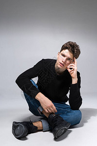 时尚英俊的男人坐在地板上摆姿势帅气的男人酷时尚男模特坐在灰色的背景上图片