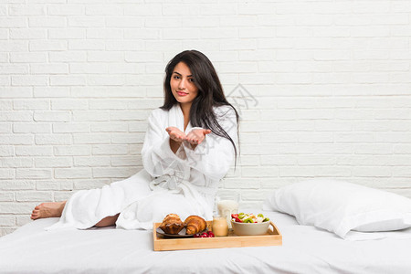 年轻的卷发女人在床上吃早餐拿着手掌拿东西图片