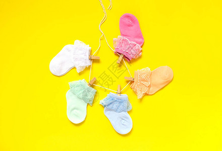 穿着黄色背景衣物的多彩可爱婴儿袜子挂在衣绳上图片