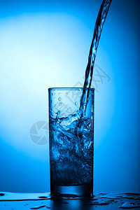 水倒进蓝色背景的玻璃杯中图片