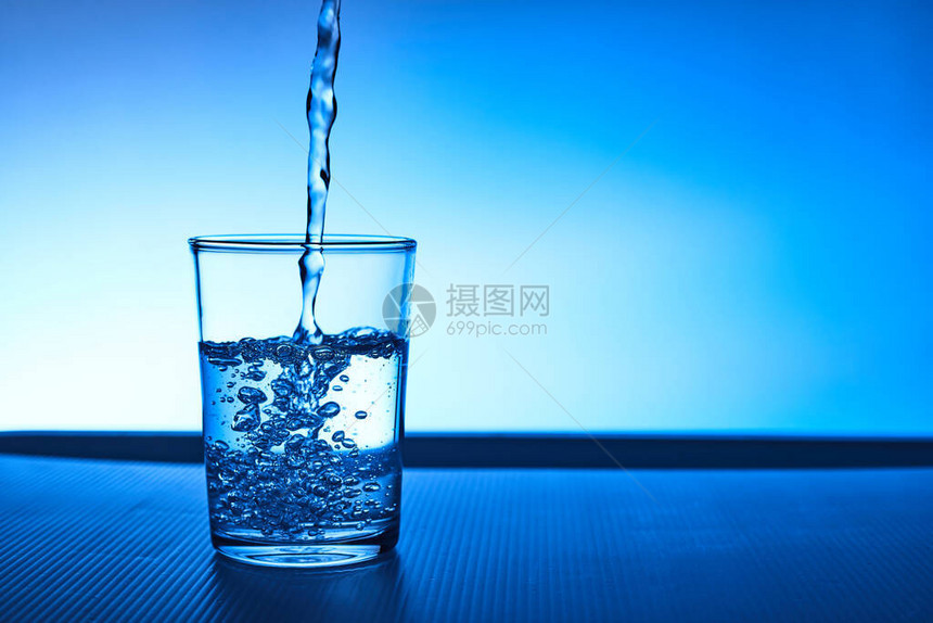 将水倒入蓝色背景的玻璃杯中图片