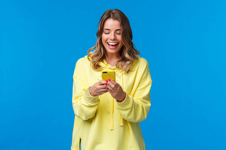 快乐微笑的金发女孩在黄色外壳中使用手机图片