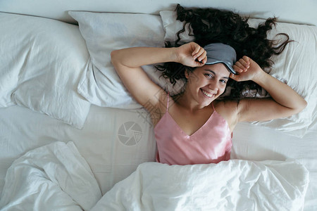 在明亮的早晨醒来的女人睡眠面膜白床单图片