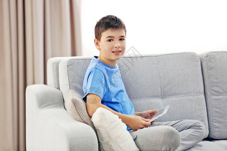 有平板电脑的男孩坐在家里的沙发上图片