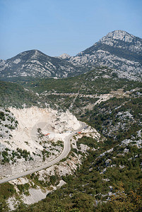 山坡荒地上有绿树和高山景色的山上蛇纹山路图片