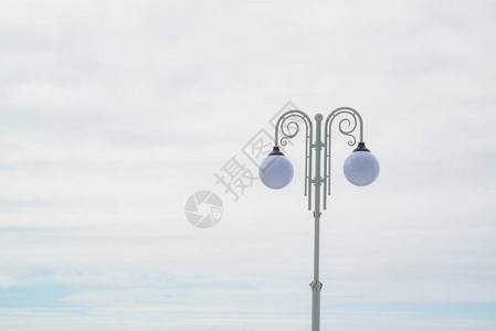 白色旧柱子上的两盏球形街灯在光天空背景上图片