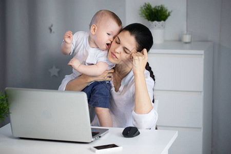 疲倦的困苦母亲试图怀着一个反复无常的孩子在她怀里工作图片
