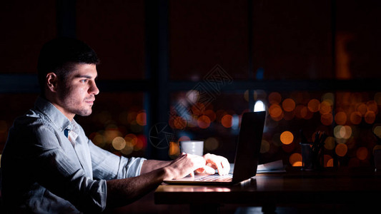 现代办公室近窗处的青年商人在笔记本电脑上加班工作图片