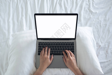 女坐在床上使用并空白桌面屏幕键盘在笔记本电脑上打字的妇女的图片