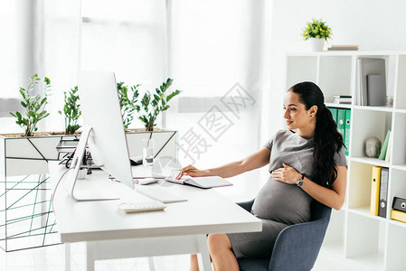 孕妇与书架和花盆一起坐在房间里图片