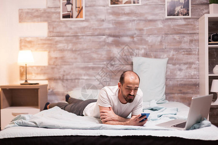 晚上躺在床上的男人穿着睡衣检查智能手机图片