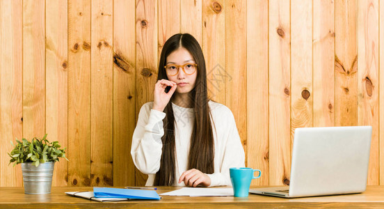 年轻的女人在她桌上用手指在嘴唇上学图片