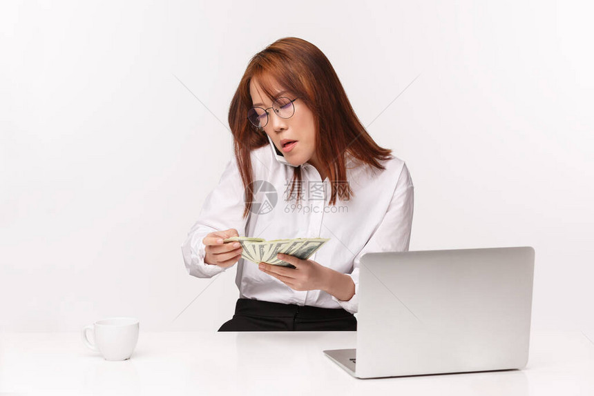 职业工作和女企业家的概念忙碌严肃的亚洲女商人办公室女士坐桌数钱在手机上交谈在笔记本电脑上写图片