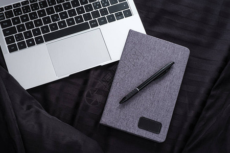 笔记本电脑和带笔的记本在床上酒店在黑色床单背景上图片