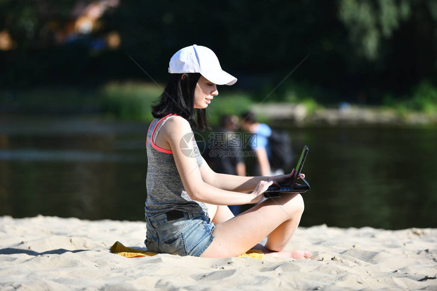 年轻妇女坐在牛仔裤短上在海滩与图片