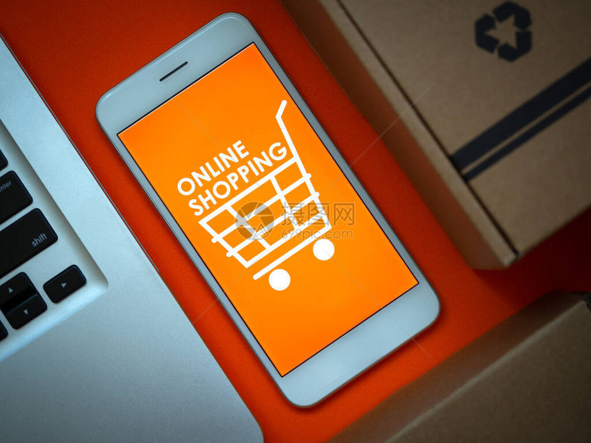 网上购物的概念特写词在线购物和智能手机屏幕上橙色背景上的购物车图标和笔记本电脑上的橙色背景平躺图片