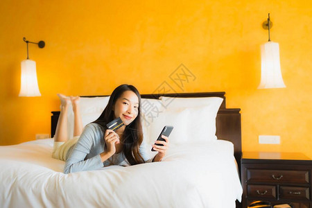 使用带信用卡的手机在卧室在线购物的美丽亚洲图片