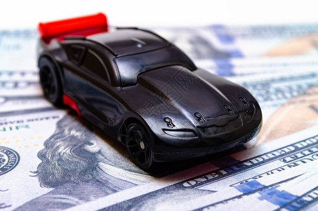 白色和黑色背景上一堆美元钞票上的黑色玩具车图片