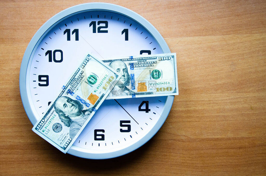 模拟时钟和木制背景上的美元钞票以箭头的形式躺在时钟上100美元表示小时和分钟从上面查看在时钟间20图片