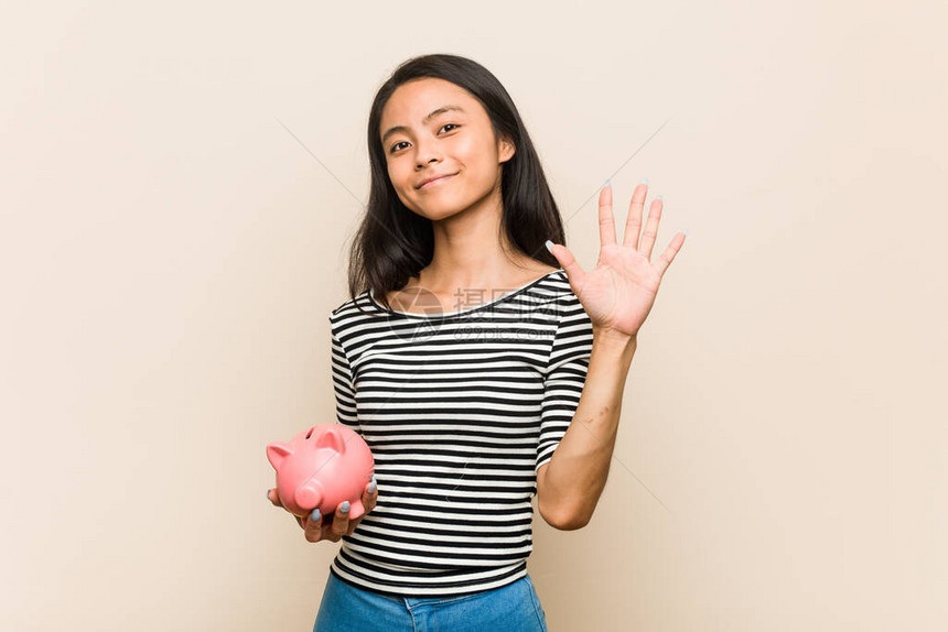 年轻的亚洲女人拿着小猪银行微笑着快乐的笑容展图片