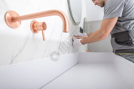 白种人杂工人用手将铜色水龙头固定在浴室的大理石瓷砖墙上图片