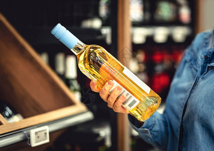白酒瓶在手酒类商店顾客买酒女人选择合适的一瓶霞多丽或雷司令酒精饮料过道和超市货架图片