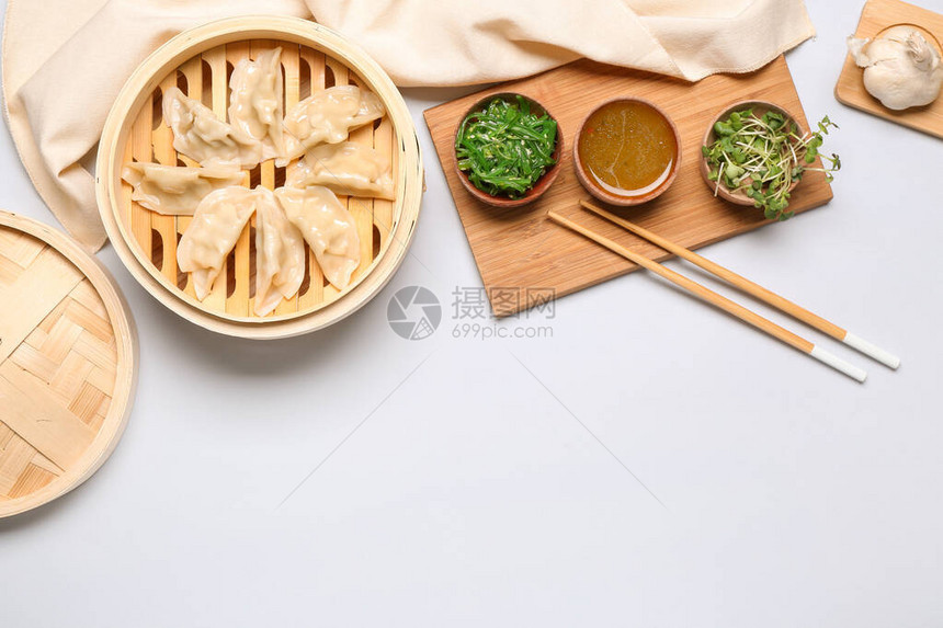 白色背景中带有美味日本饺子的竹蒸笼图片