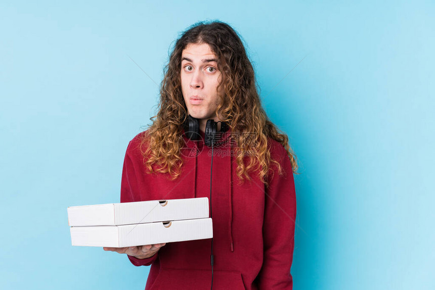 年轻caucasian男子拿着披萨孤立的肩膀和睁开的图片