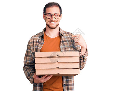 年轻英俊的caucasian年轻男子拿着送披萨盒指着一个笑着快乐图片