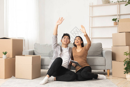 亚洲家庭仰望着坐在新公寓的地板上装着移动箱子梦想着图片