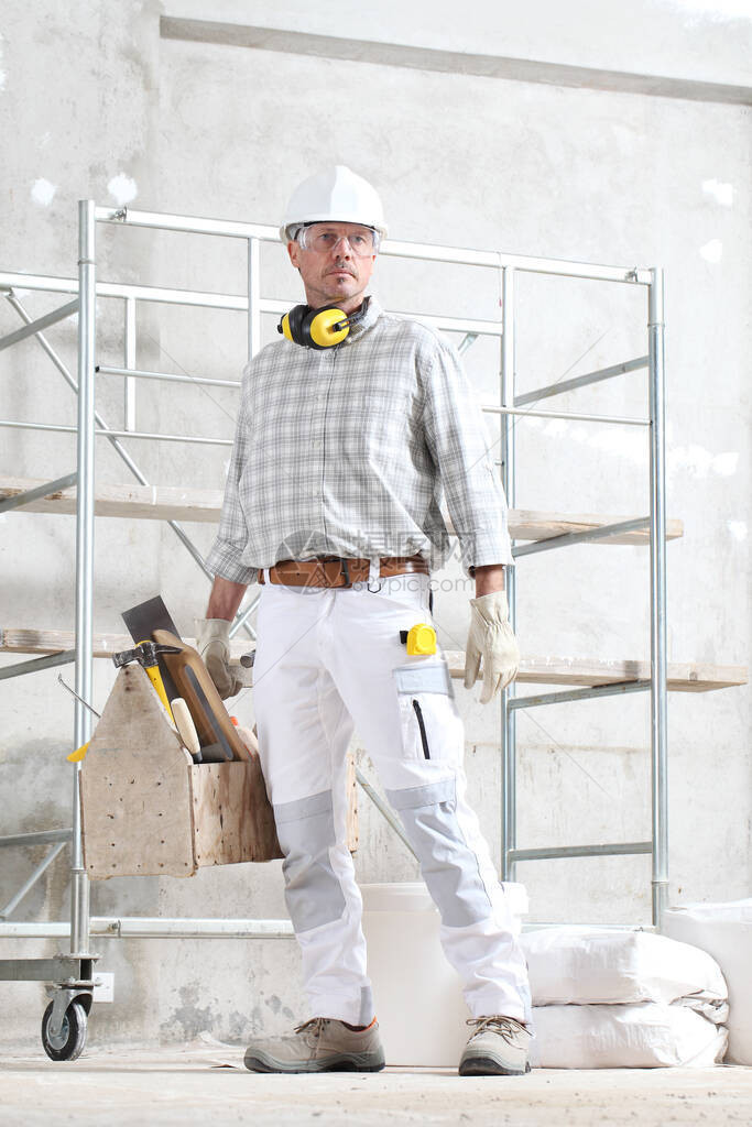 手持工具箱的男建筑工人戴手套安全帽眼镜和听力保护耳机图片