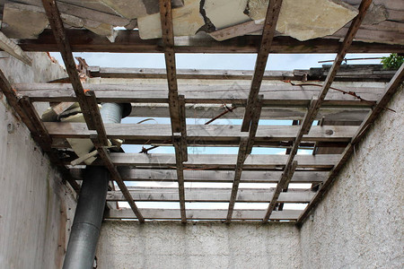 在废弃工业建筑群内用吊挂金属管和破旧墙壁隔热断碎并被毁的木板天花板图片