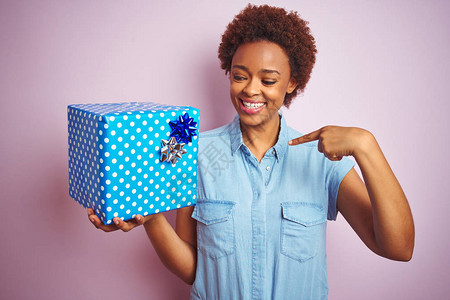 非洲裔美国妇女在粉红色的孤立背景上拿着生日礼物图片
