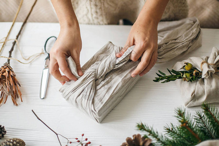 用天然冷杉草本植物松果和剪刀在白色质朴的桌子上用亚麻织物包裹圣诞礼物图片
