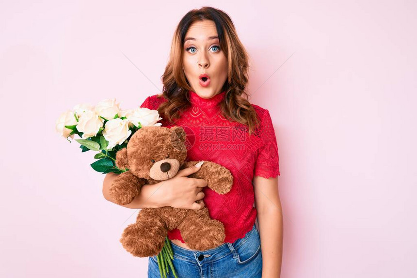 年轻漂亮的白种女人拿着熊和一束鲜花庆祝周年纪念图片