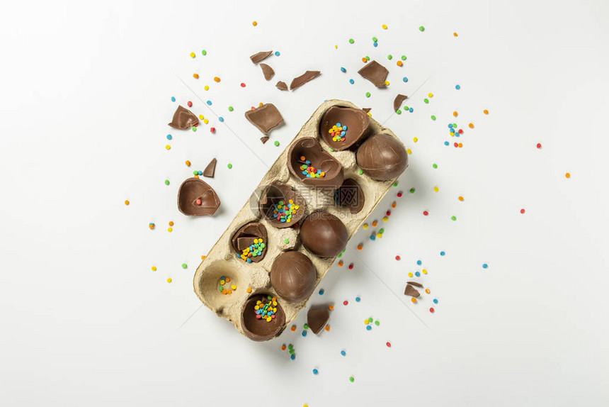 托盘上有破碎的复活节巧克力蛋和浅色背景上的多色甜糖果装饰图片