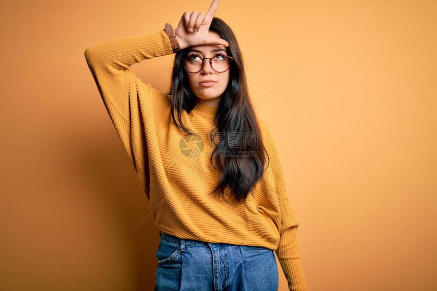 穿着眼镜和散装毛衣的年轻黑发女人在孤立的背景上取笑前额有手指的人做失败者姿态嘲弄和侮辱他们图片