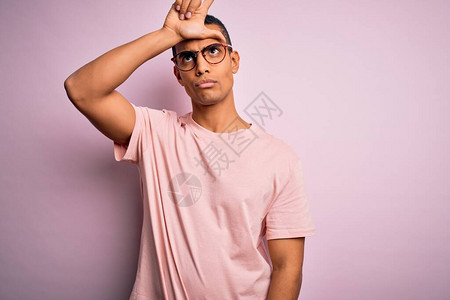 身穿轻便T恤和眼镜的非洲帅哥在粉红色背景上取笑前额有手指的人图片