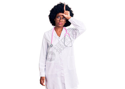 身着医生大衣和听诊器的年轻非洲女取笑前额有手指的人图片