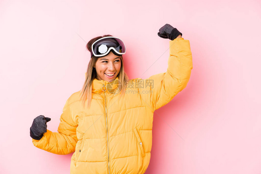 年轻的caucasian女人穿着粉红色的滑雪衣在胜利后举图片