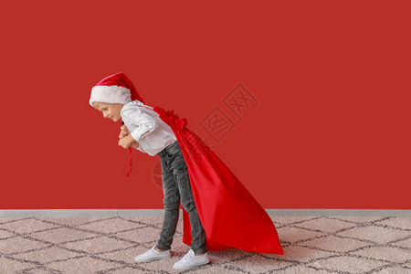 穿着圣诞老人帽子的可爱小男孩带着礼物在彩色图片