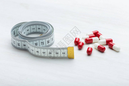 红色和白色的减肥药放在卷尺旁边的白色桌子上借助药背景图片