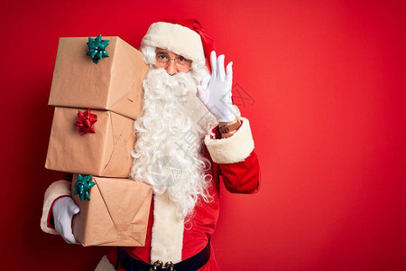 身穿圣诞老人服装的老人在孤立的红色背景上拿着礼物塔图片