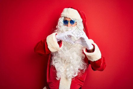 身着圣诞老人服装和太阳镜的中年男子在孤立的红色背景上笑着爱图片