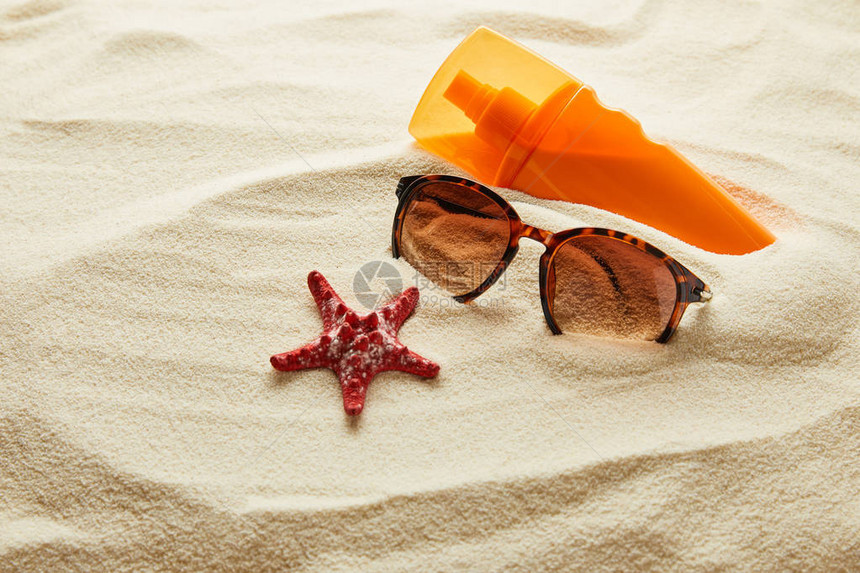沙子上有红海星和橙色瓶子防晒霜的棕褐色时图片