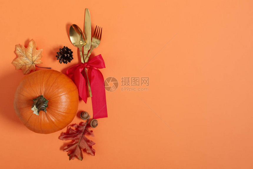 与餐具南瓜和其他秋天装饰品一起的感恩节晚宴表在橙色背景的图片