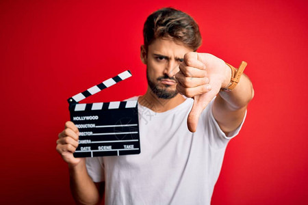 留着胡须的年轻导演在孤立的红色背景上用隔板制作电影图片
