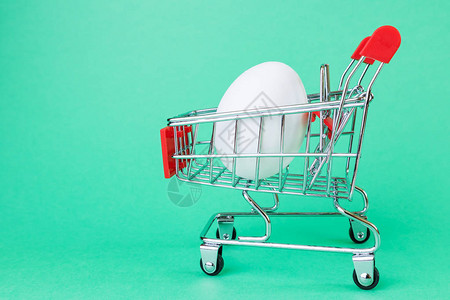 绿色背景上的超市购物篮的小副本里面是一个白色的鸡蛋购物杂货店折扣图片