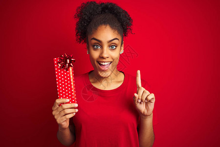年轻的非洲裔美国女在孤立的红色背景下拿着情人节礼物图片
