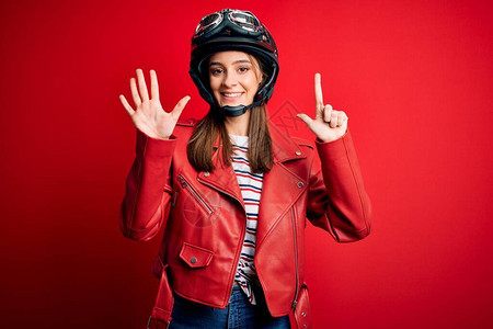 年轻漂亮的黑发摩托车手女人戴着摩托车头盔和红色夹克图片